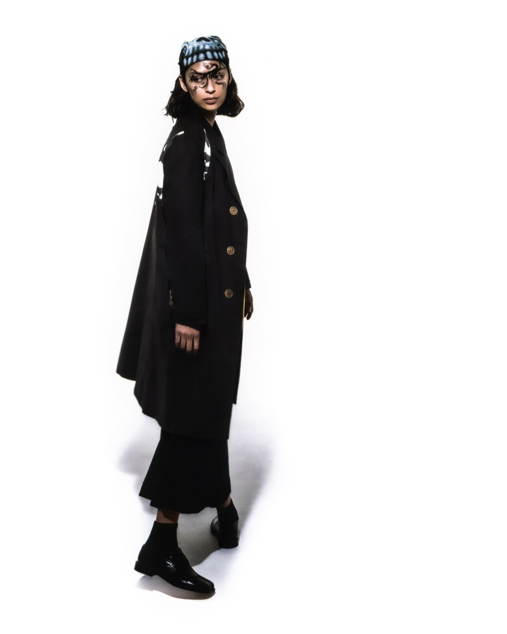 Model wearing glack graphic liner, a long black coat and bandana against a white background